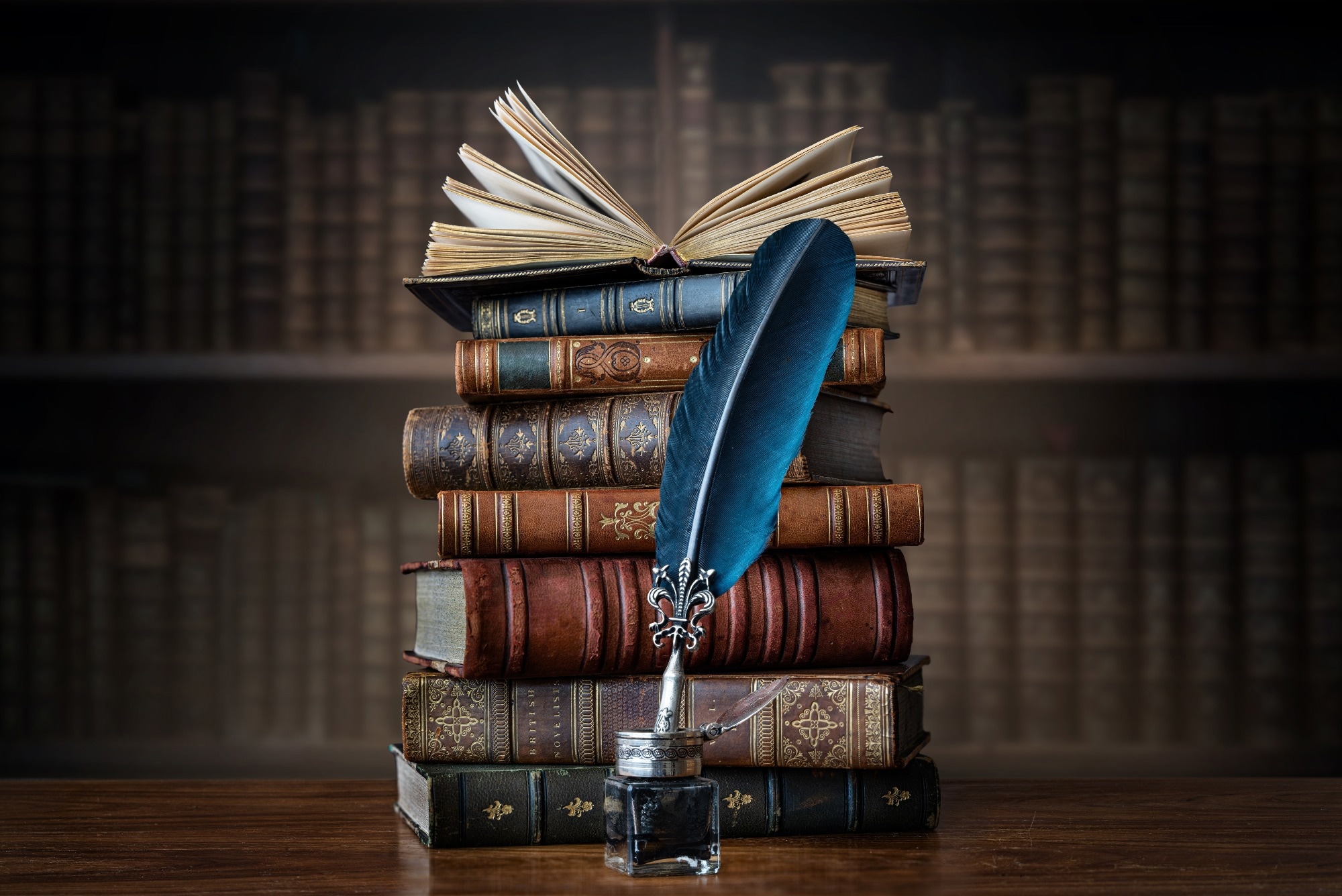 Old books, quill pen and vintage inkwell on wooden desk in old library.