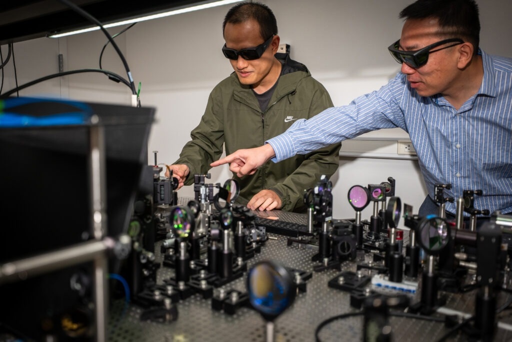 Postdoctoral fellow Tianwei Wu (left) and Professor Liang Feng (right) in the lab, demonstrating some of the apparatus used to develop the new, light-powered chip. (Credit: Sylvia Zhang)