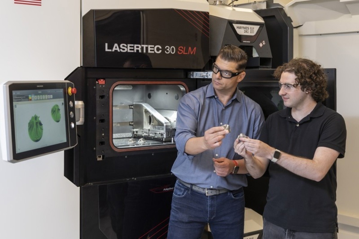 Credit: Rowan University Antonios Kontsos, Ph.D., director of Rowan University’s Digital Engineering Hub, and mechanical engineering senior Sam Menaker work with the lab’s key piece of equipment, a 3D metal printer connected to a supercomputer. The team works to integrate intelligent systems with real-world manufacturing methods.